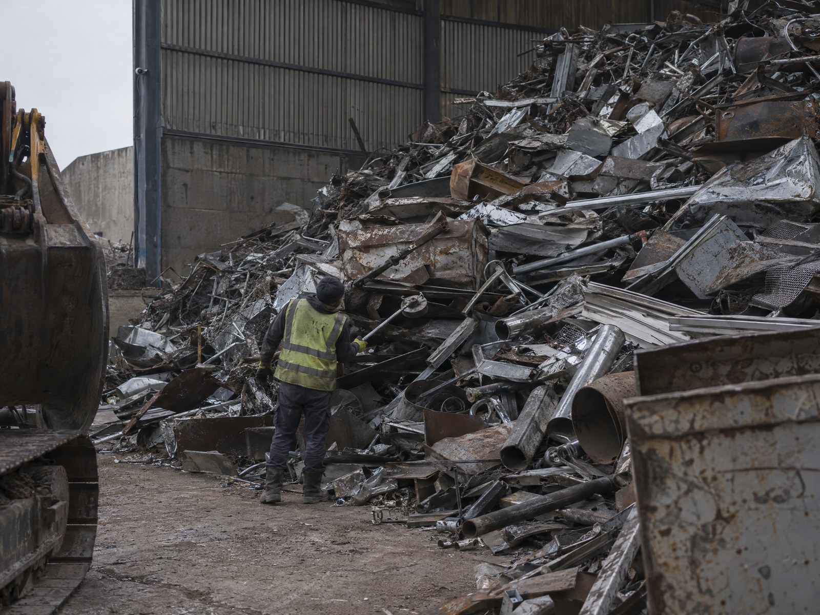 Illustrative heap of mixed scrap metal with a worker standing at the edge of the pile.